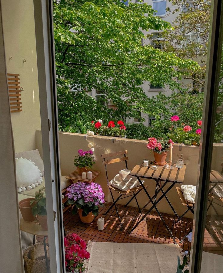 an open door leading to a balcony with flowers on the table and chairs in it