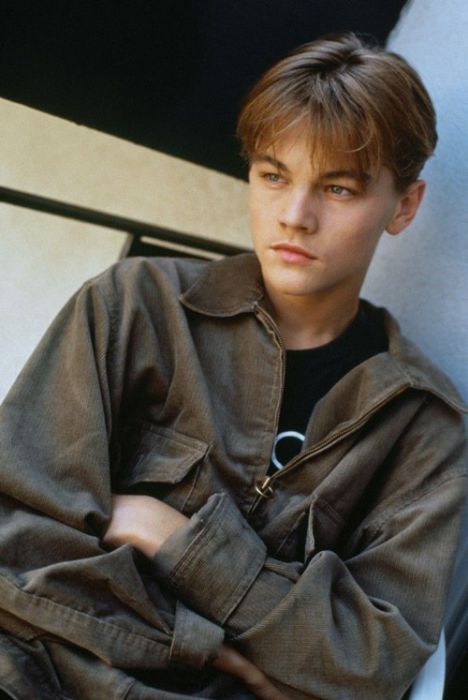 a young man leaning against a wall with his arms crossed and looking at the camera