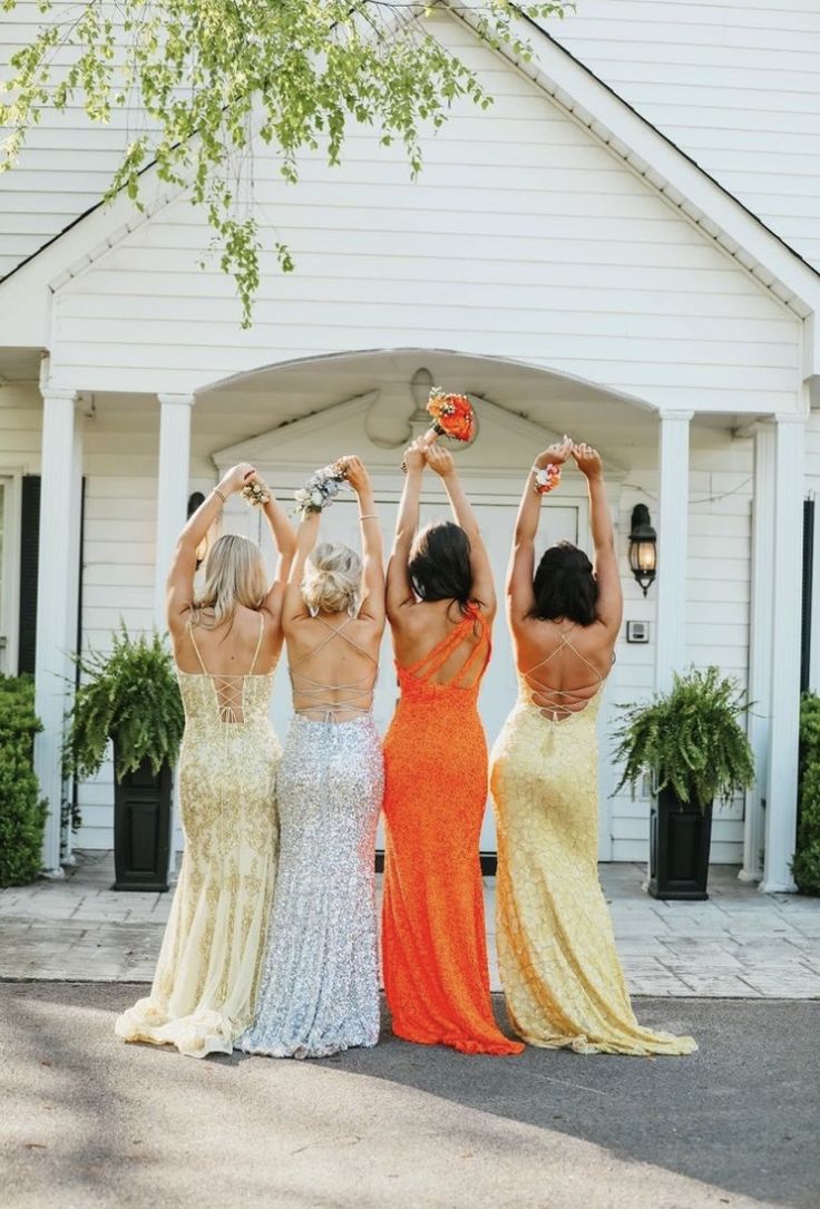 three women in long dresses are holding their hands up above their heads and looking at the sky