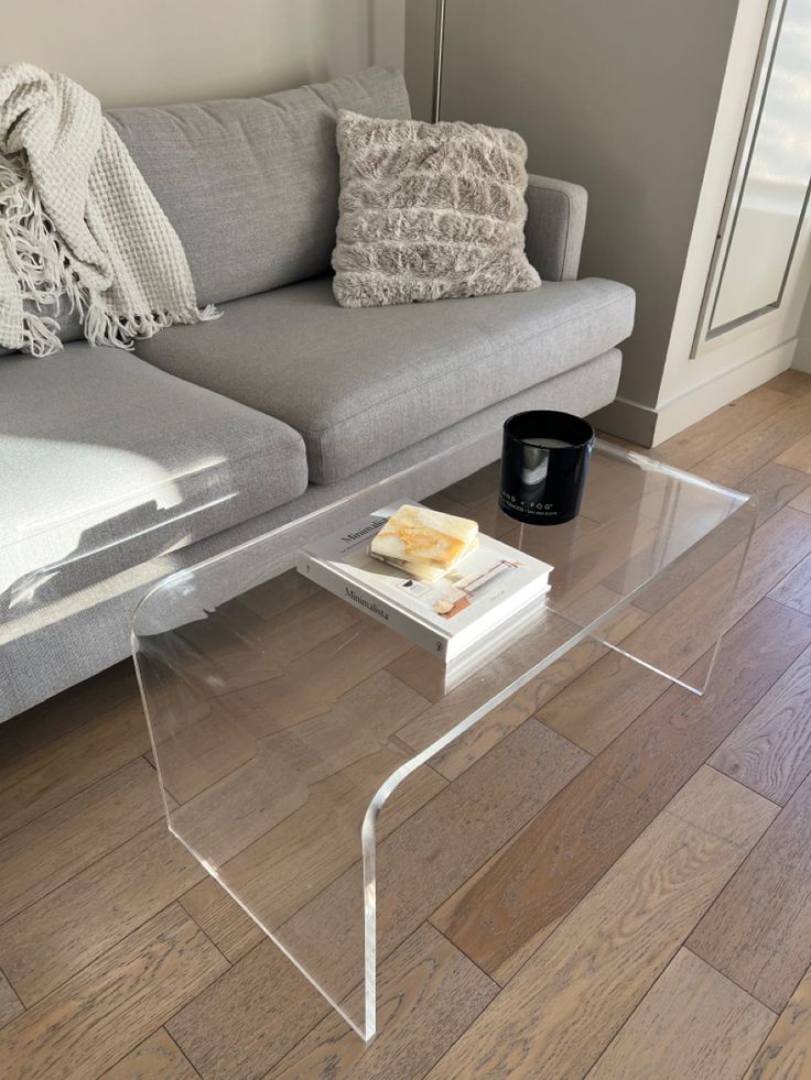 a glass coffee table sitting on top of a wooden floor next to a gray couch