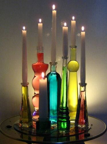 there are many different colored glass bottles with candles in them and one is lit up