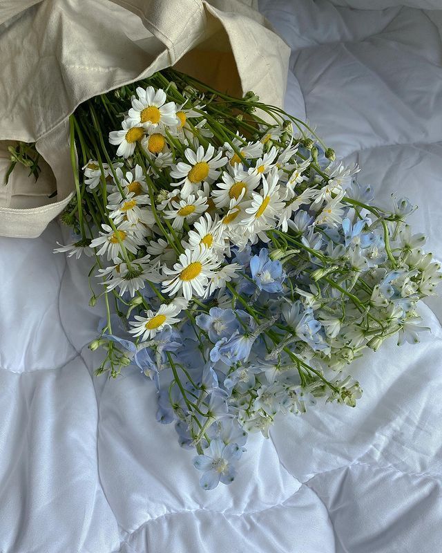 a bouquet of daisies and wildflowers on a white bed sheet with a tote bag in the background