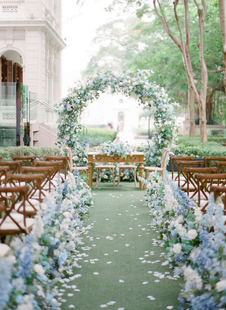 an outdoor wedding ceremony with blue and white flowers on the aisle, surrounded by greenery