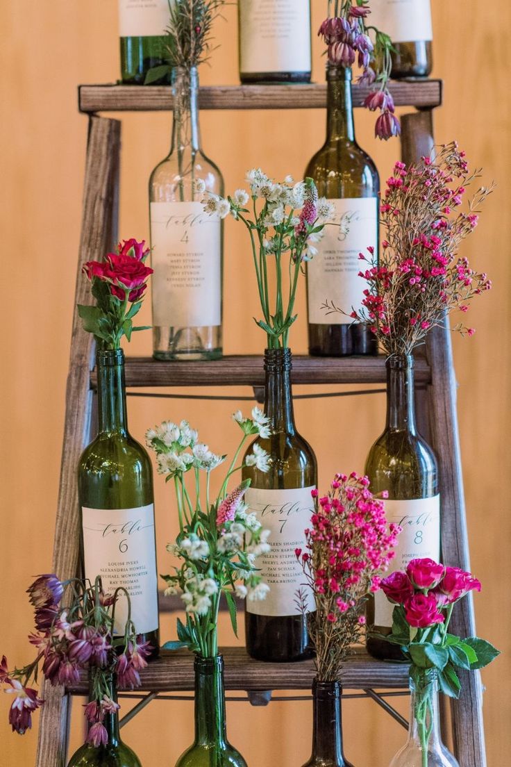 several wine bottles with flowers in them sitting on a wooden shelf next to a ladder