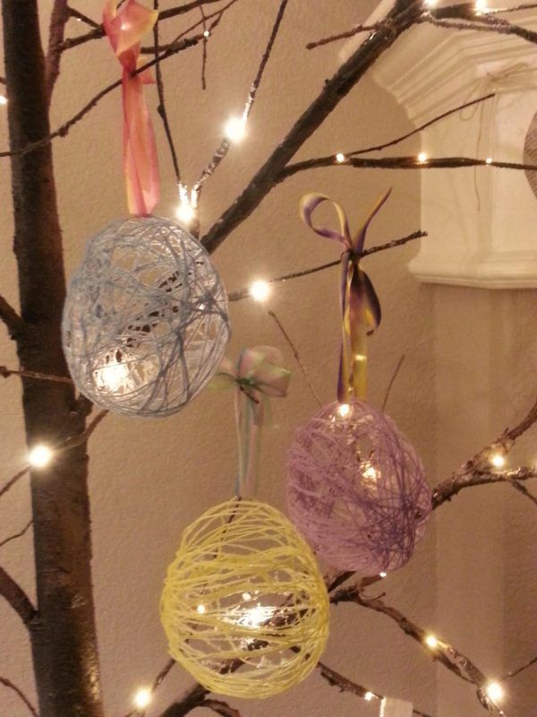 three ornaments are hanging from a tree with lights on the branches in front of it