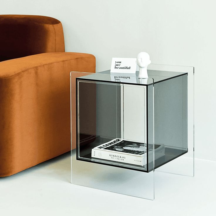 a glass table with a book on it next to an orange chair and couch in the background
