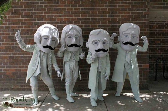 five people with fake moustaches standing in front of a brick wall