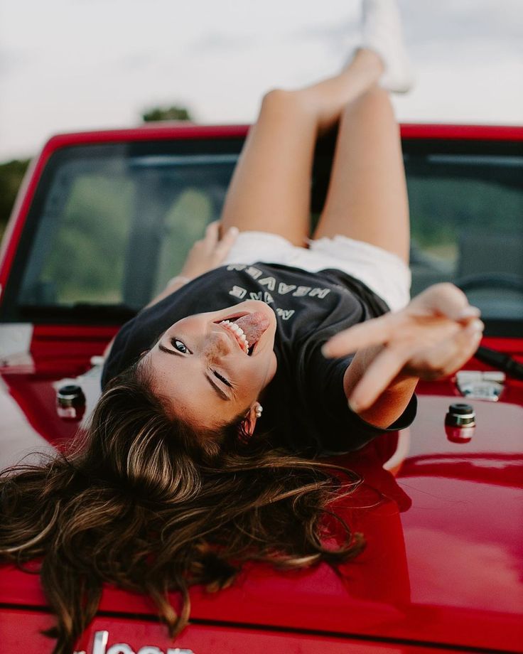 a woman laying on the hood of a red truck with her feet up in the air