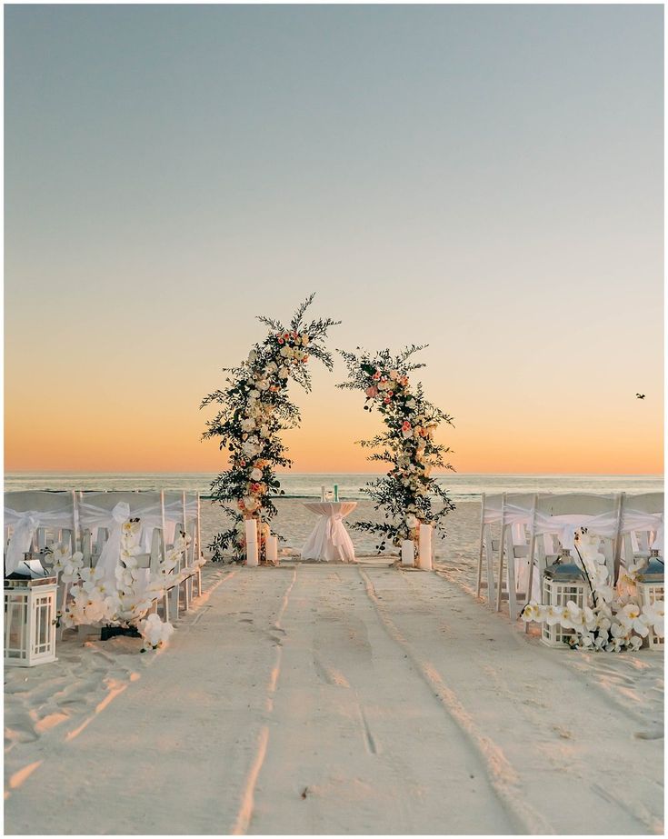 an outdoor ceremony set up on the beach with white linens and floral arch decorations