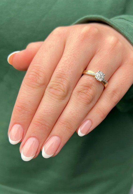 a woman's hand with white and pink manicured nails holding a diamond ring
