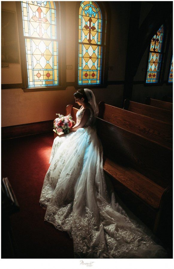 a woman in a wedding dress sitting on a bench next to a stained glass window
