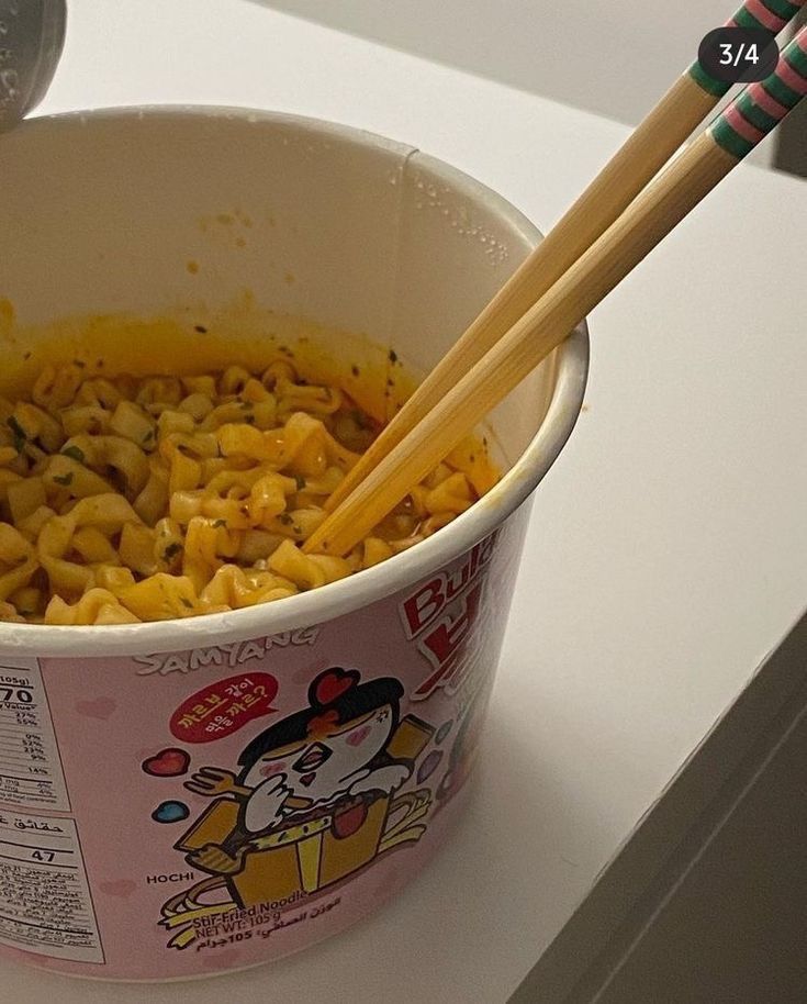 two chopsticks sticking out of a bowl of macaroni and cheese on a counter