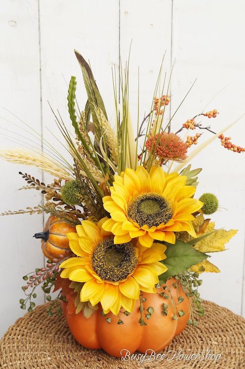 a pumpkin vase filled with sunflowers and other fall flowers sitting on top of a straw hat
