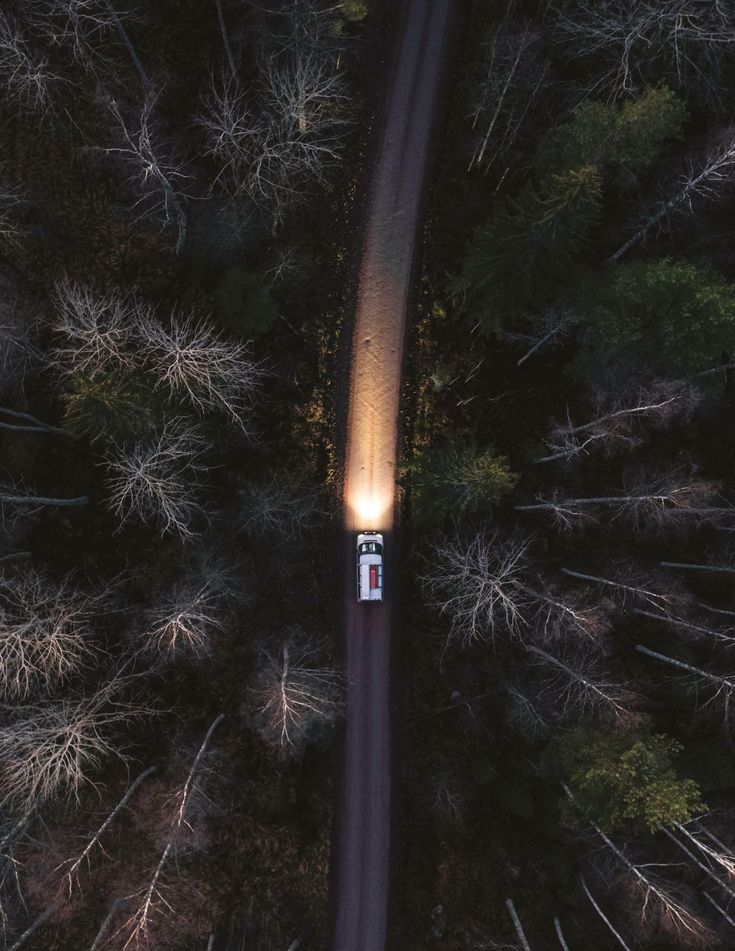 an aerial view of a car driving down a road in the woods at night with its headlights on