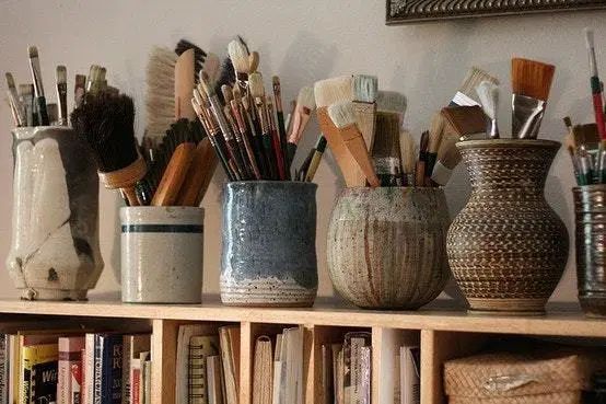 there are many vases with brushes in them on the shelf next to each other