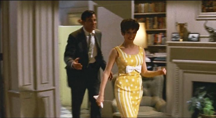 a woman in a yellow and white dress walking past a man in a black suit