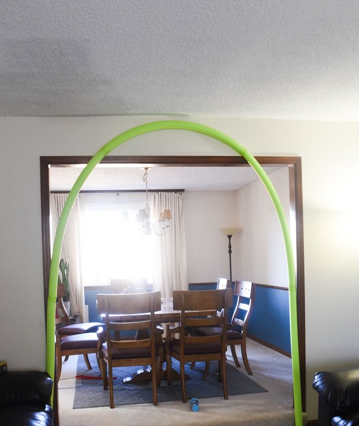 a dining room table with chairs and a green arch in the middle of the room