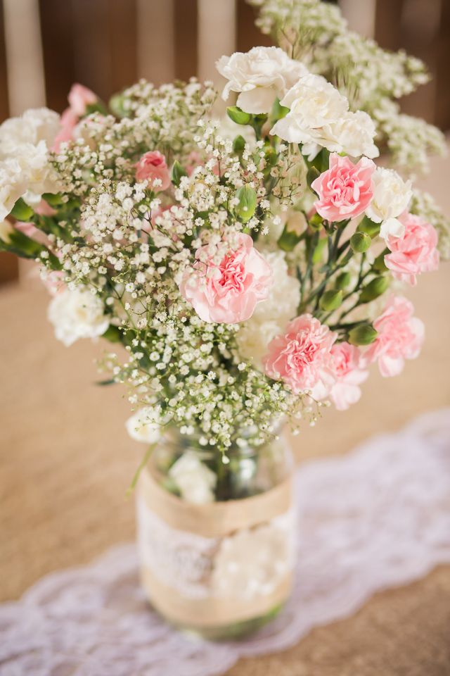 a vase filled with pink and white flowers on top of a lace covered table cloth