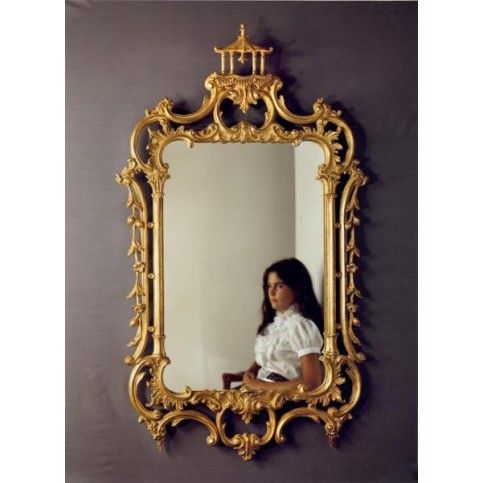 a woman is standing in front of a gold mirror with her reflection on the wall