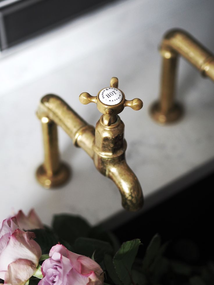 a gold faucet sitting next to pink flowers