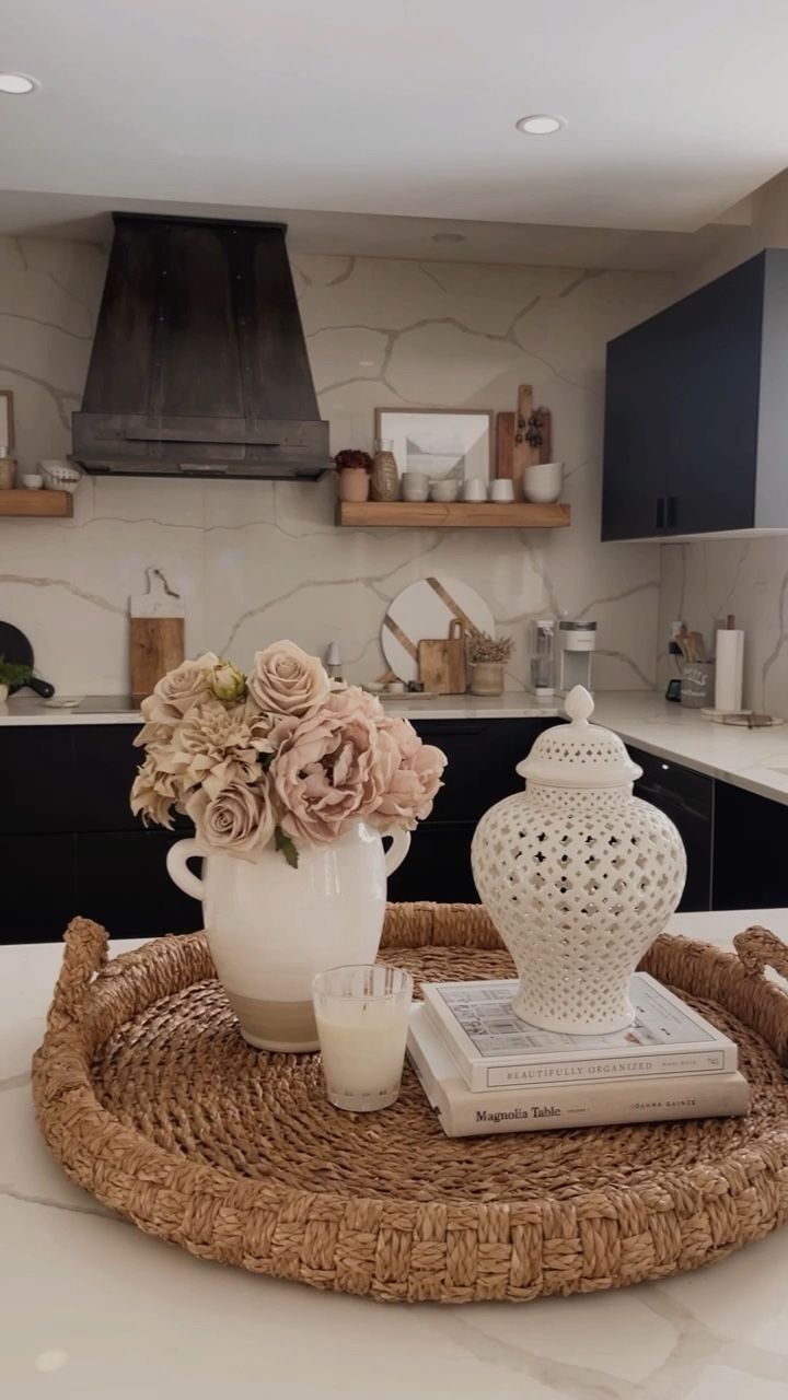 a white vase with flowers sitting on top of a wicker tray in a kitchen