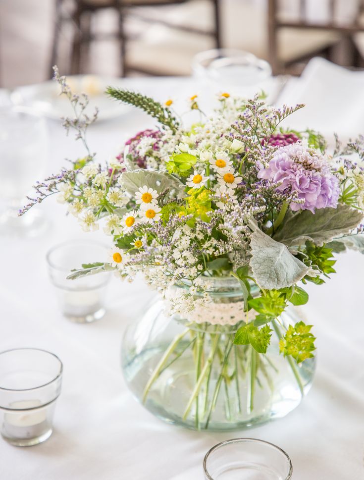 a vase filled with lots of flowers on top of a white tablecloth covered table