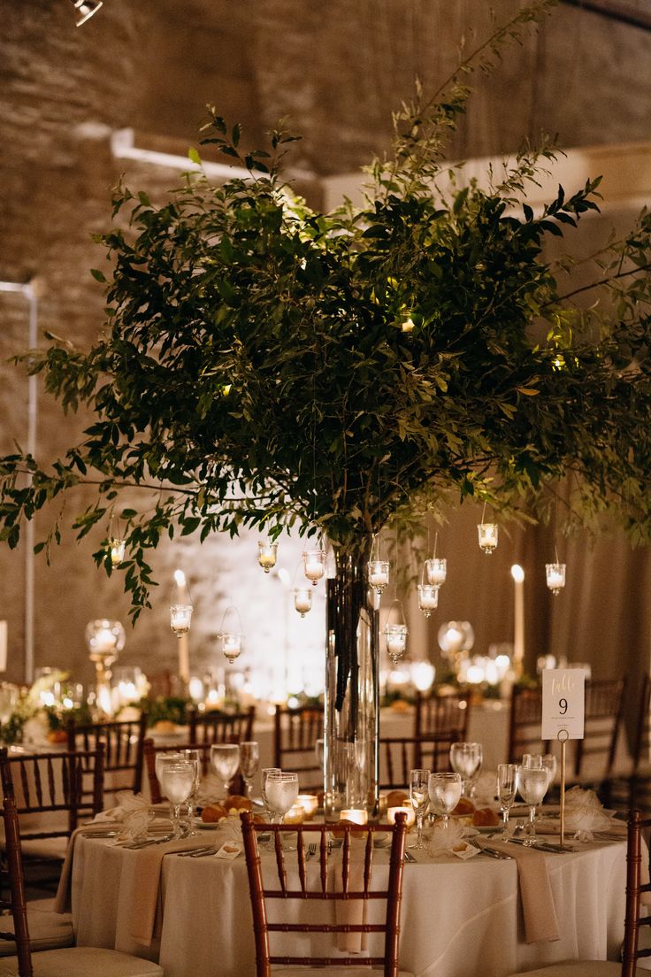 a tall vase filled with greenery sitting on top of a table covered in white linens