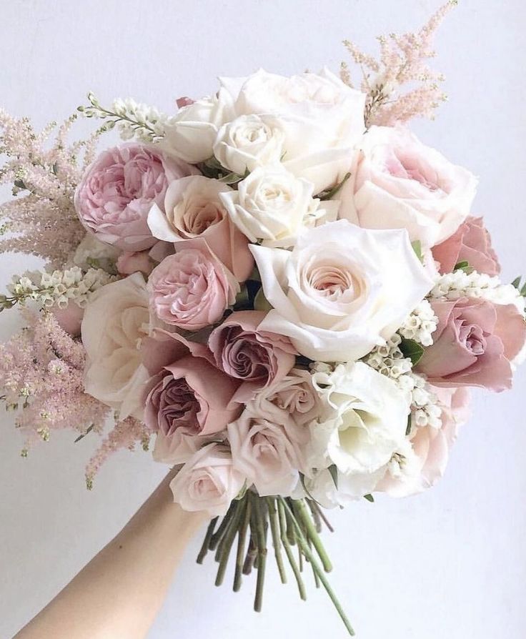 a bridal bouquet with pink and white flowers is held by a woman's hand