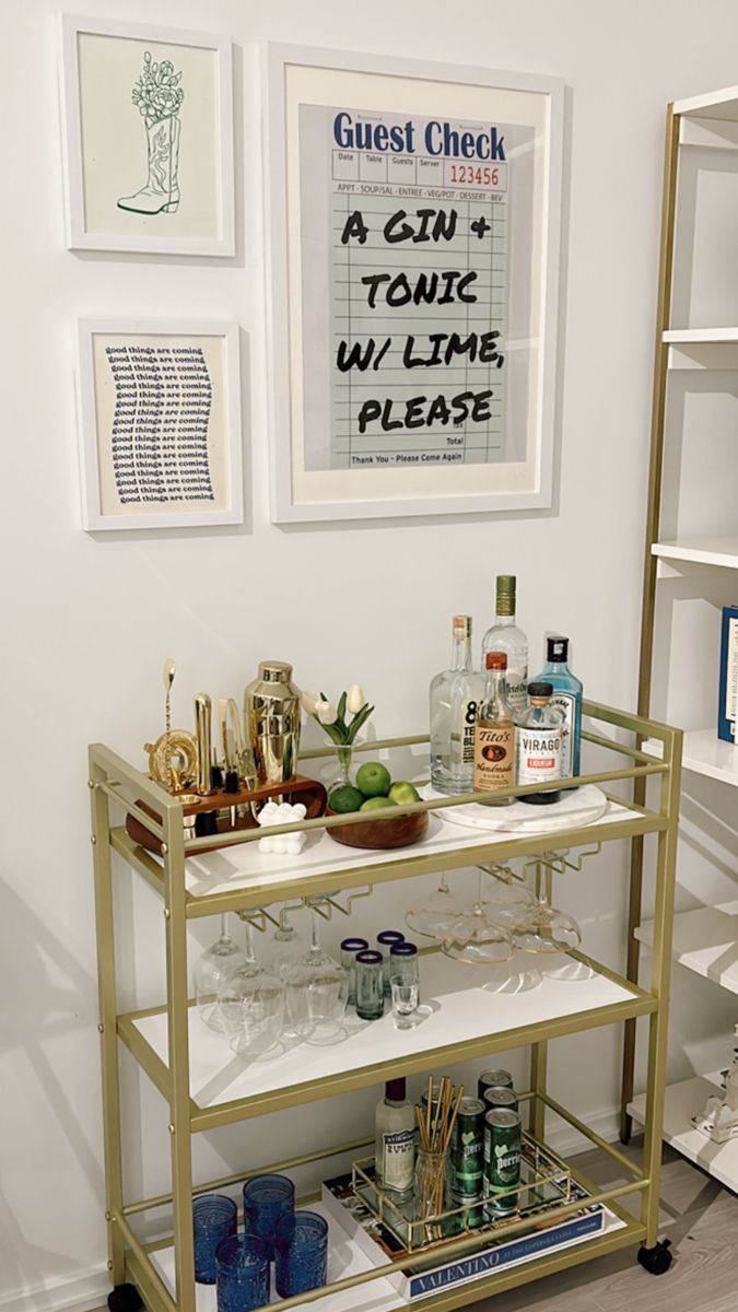 a bar cart with drinks on it in front of some framed pictures and art work
