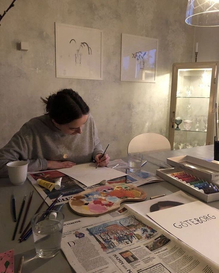 a woman sitting at a table with papers and paintbrushes in front of her