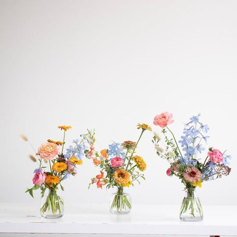 three vases filled with colorful flowers on top of a white table next to a wall