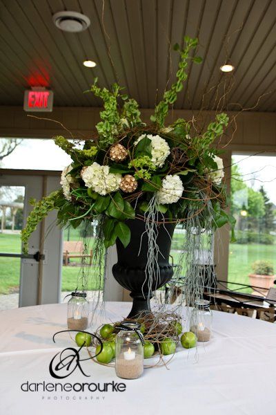 an arrangement of flowers and greenery in a black vase on a white table cloth