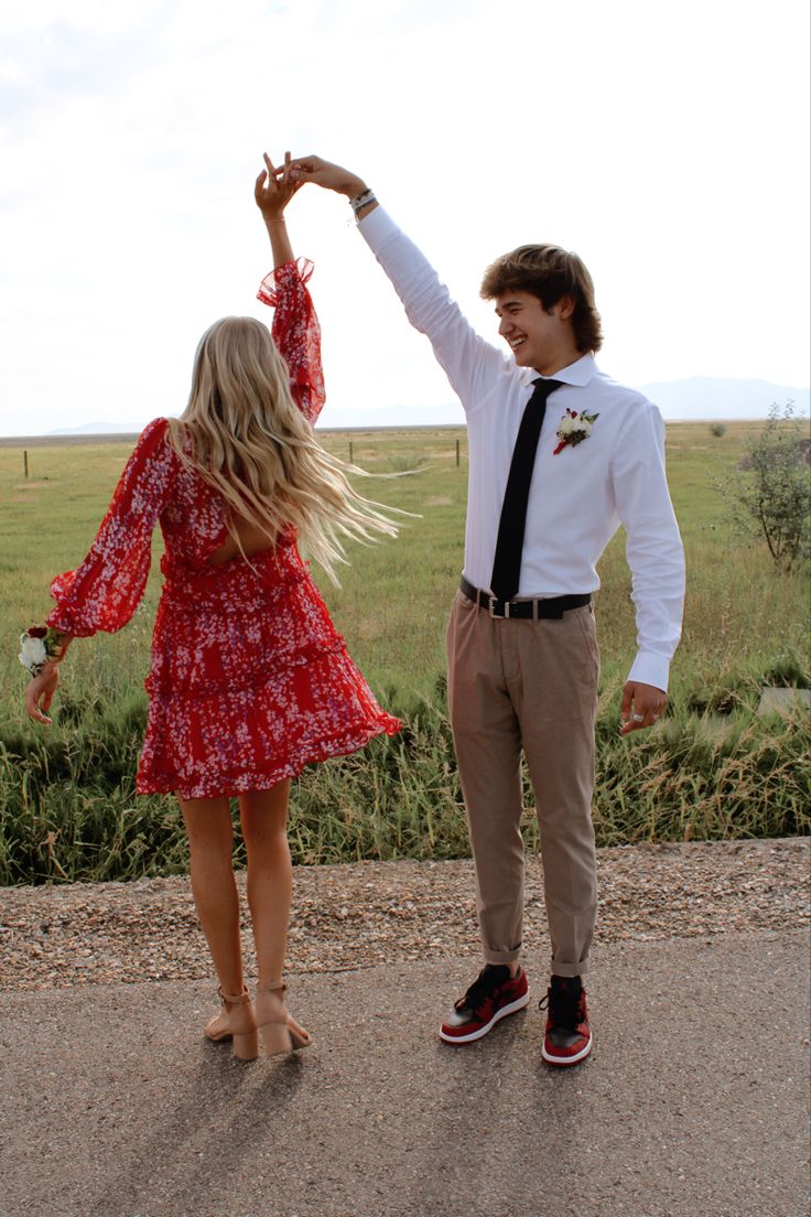 a young man and woman dancing on the side of a road in front of an open field