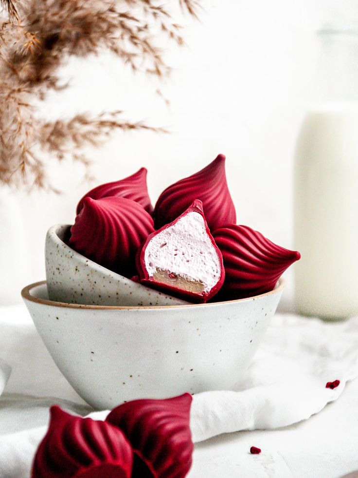 a bowl filled with red velvet hearts next to a glass of milk
