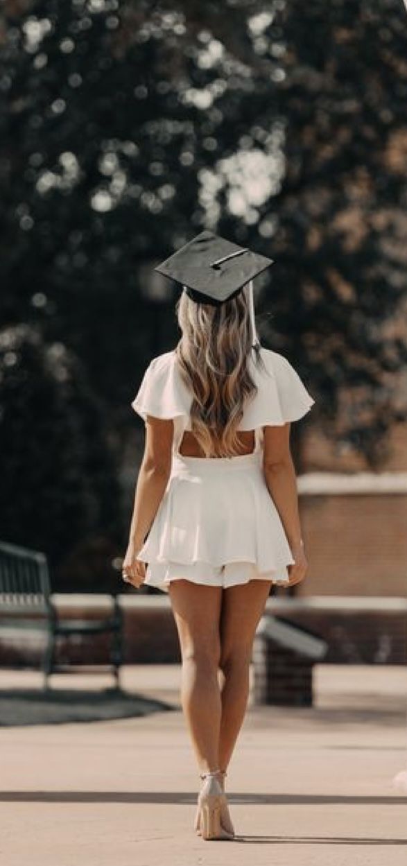 a woman in a graduation cap and dress walks down the street with her back to the camera