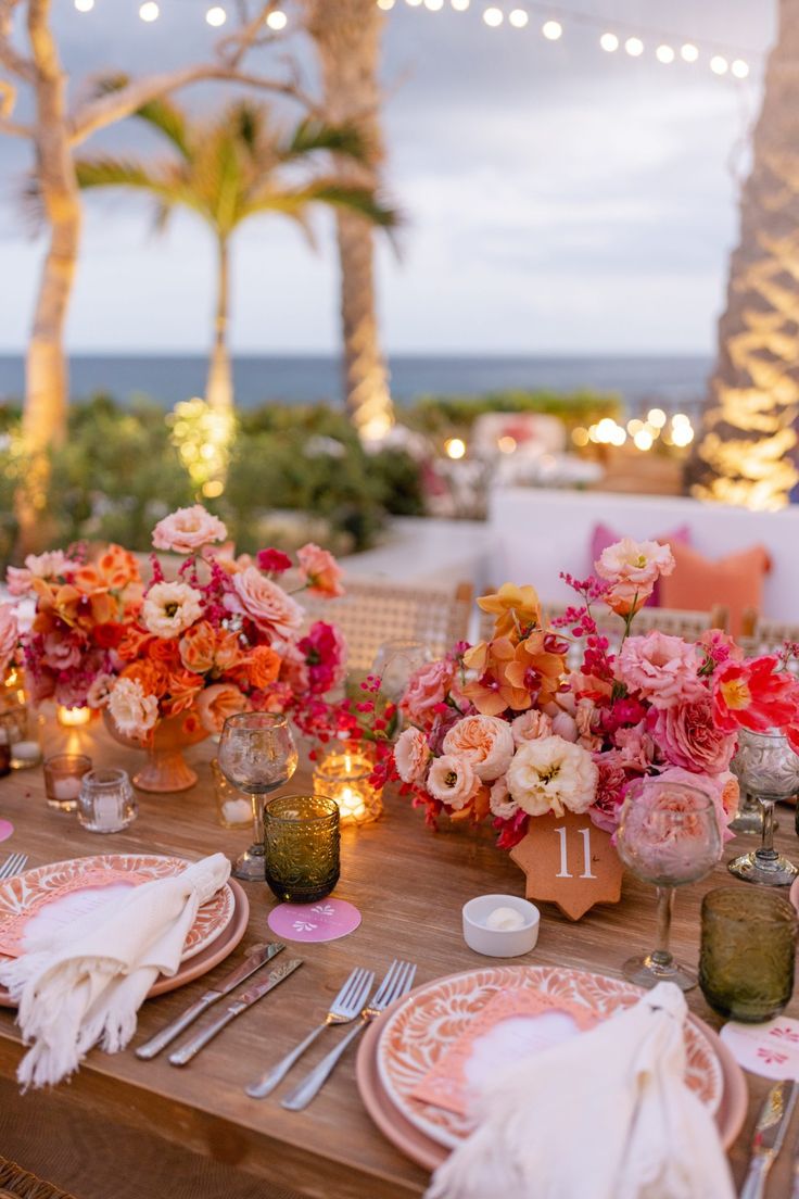 the table is set with pink and orange flowers, candles, and napkins on it