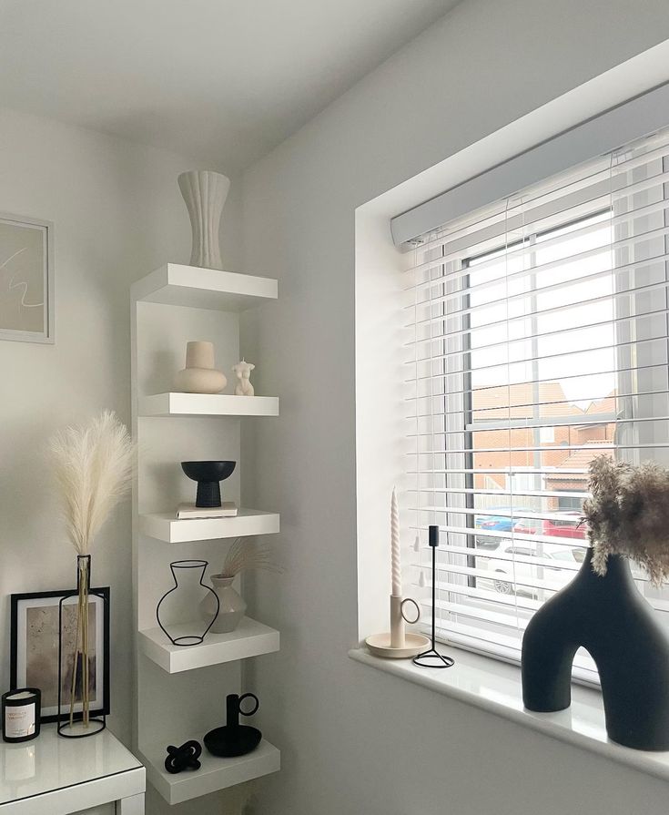 a white room with shelves and vases on the window sill next to it