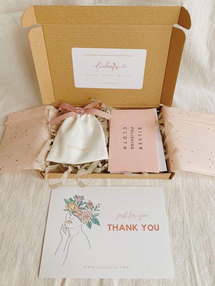 an open box with some items in it on a white sheeted surface and a thank you card