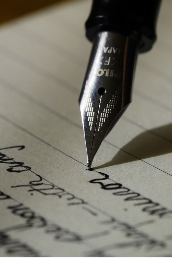 a close up of a pen on top of a piece of paper with cursive writing