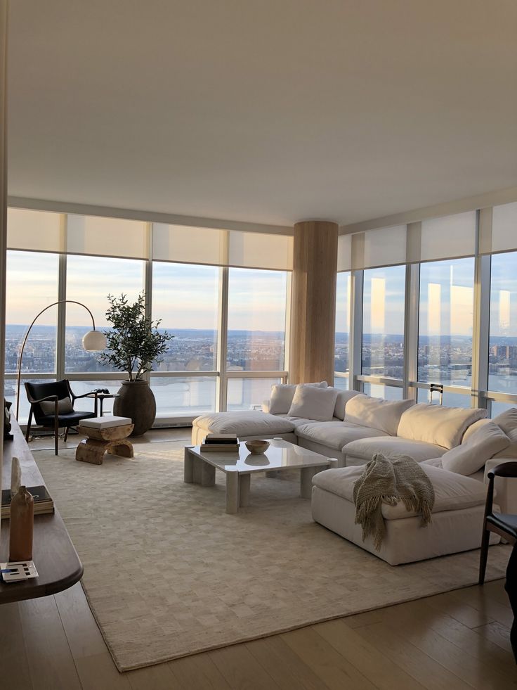 a living room filled with white furniture and large windows overlooking the cityscape in the distance