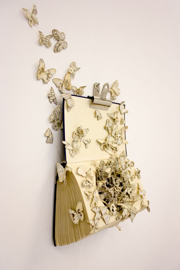 an open book with butterflies coming out of it on a white surface next to a pair of scissors