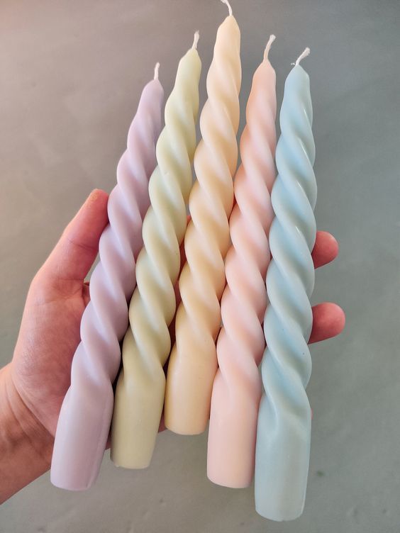a hand holding five candles in pastel colors, each with a single candle sticking out of it
