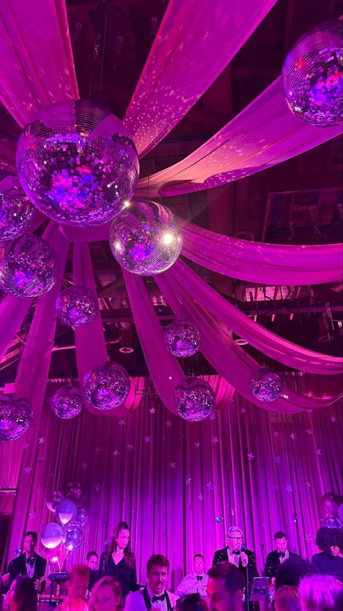 people are sitting at tables in front of purple lights and disco balls hanging from the ceiling