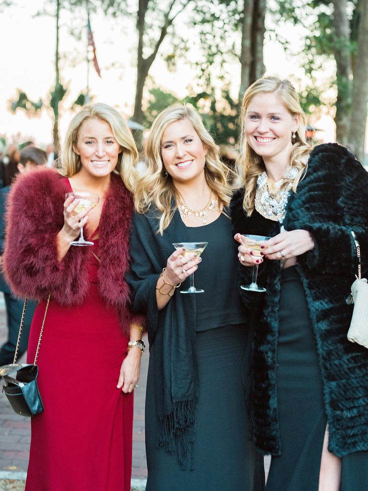 three women standing next to each other holding wine glasses