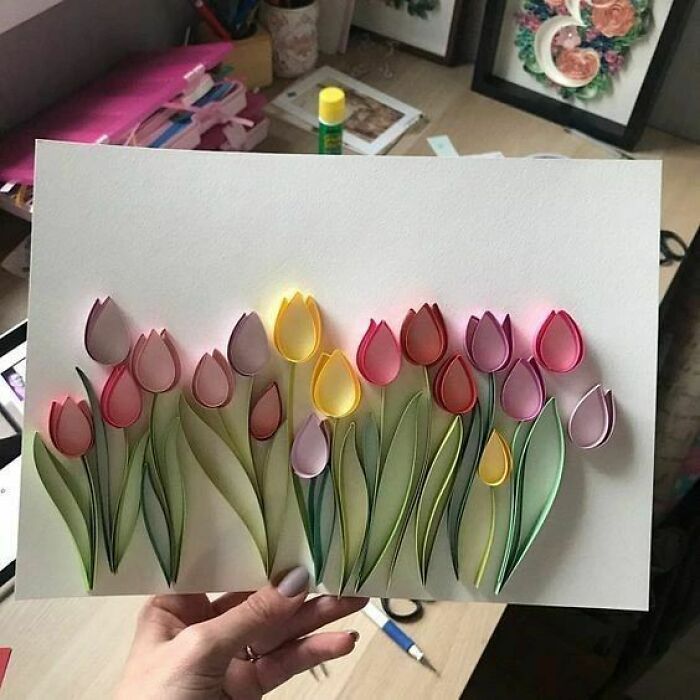 a person holding up a piece of paper with flowers cut out of it on it