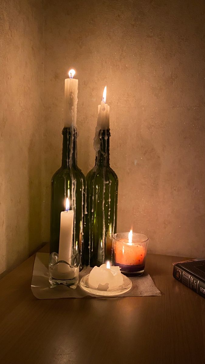 two bottles with candles are sitting on a table next to a plate and candle holder