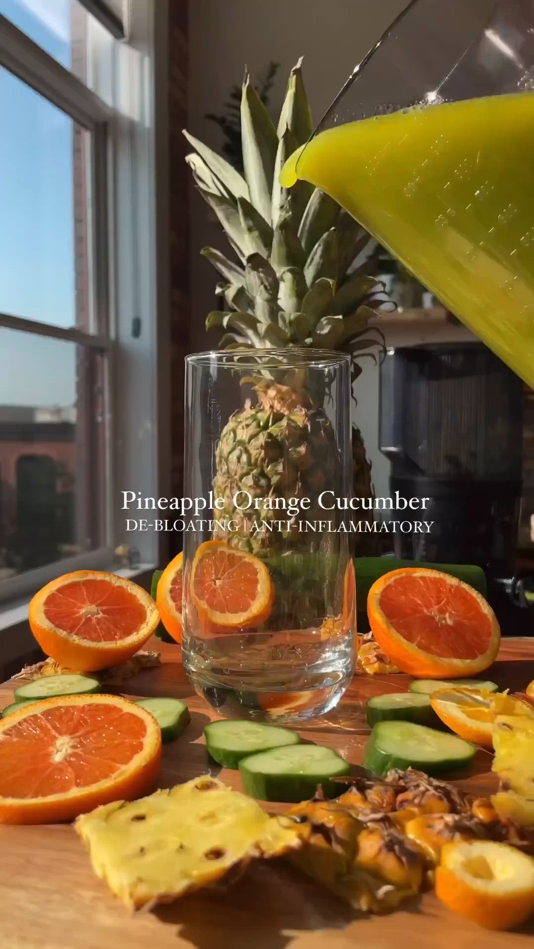 This may contain: a pineapple drink being poured into a glass with sliced oranges and cucumbers