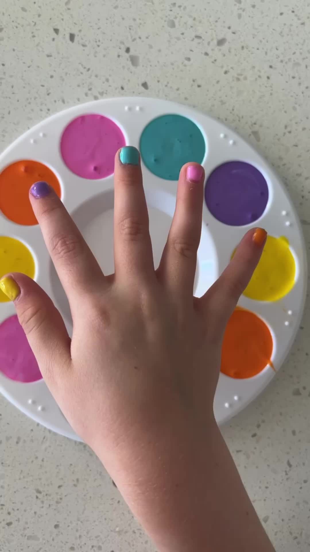 This may contain: a person's hand with multicolored nail polish sitting on top of a plate