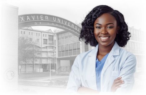 An African American woman in a white lab coat standing confidently with her arms crossed in front of the Xavier University of Louisiana entrance. She is smiling and the background features the university campus.