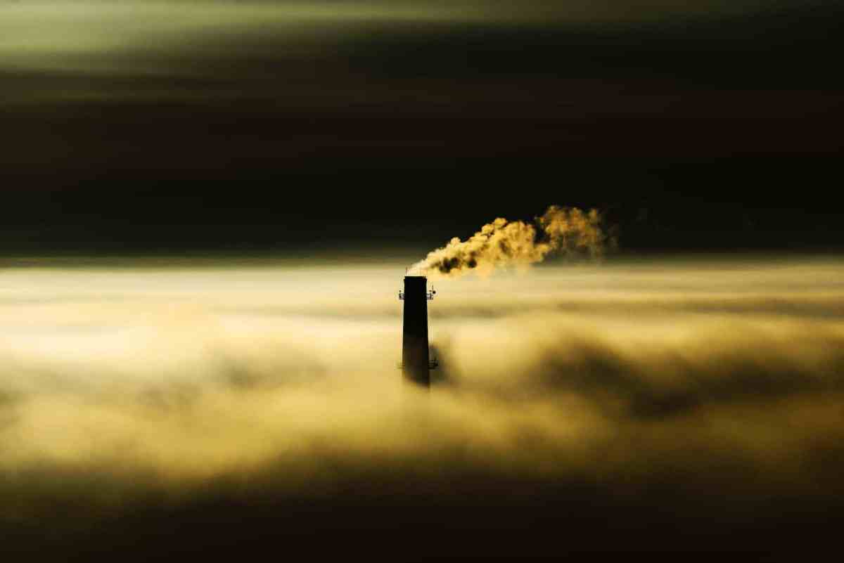 an industrial chimney over a thick fog emitting smoke